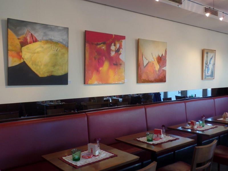 Foto: Tische und Bänke in einem Café. An der Wand hängen Bilder.